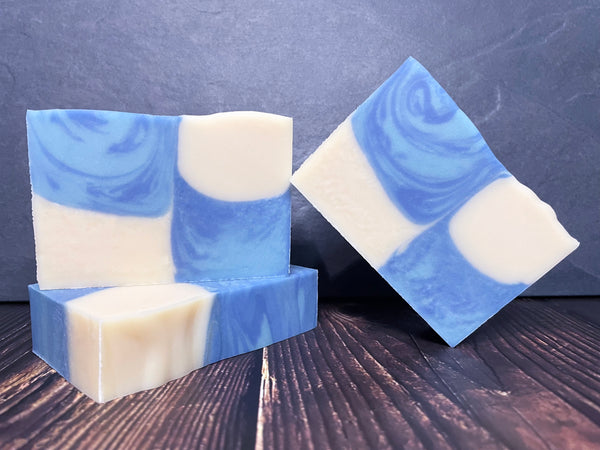 Blue and white swirled checkered beer soap bars on a wooden surface with a dark stone background