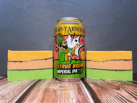 can of saint arnold citrus Boom Imperial IPA between two bars of layered green peach and gold beer soap on wooden surface