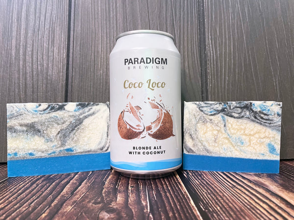 Paradigm Brewing Coco Loco beer can on a wooden surface between two bars of black blue and white beer soap