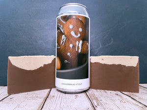 Can of gingerbread stout from evil twin brewing nyc with a gingerbread man design between two bars of brown gingerbread beer soap on a wooden surface.