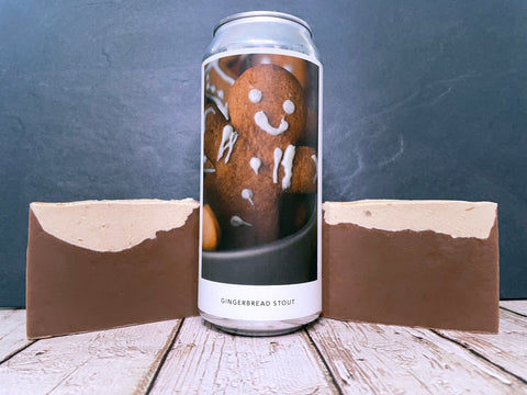 Can of gingerbread stout from evil twin brewing nyc with a gingerbread man design between two bars of brown gingerbread beer soap on a wooden surface.