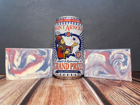 Saint Arnold Grand Prize beer can with two marbled red white and blue beer soap bars on a wooden surface.