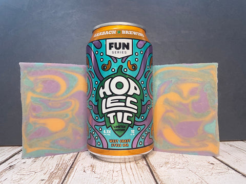 Hoplectic by Karbach Brewing Company beer can between two bars of marbled purple orange and teal beer soap on a wooden surface with a dark background