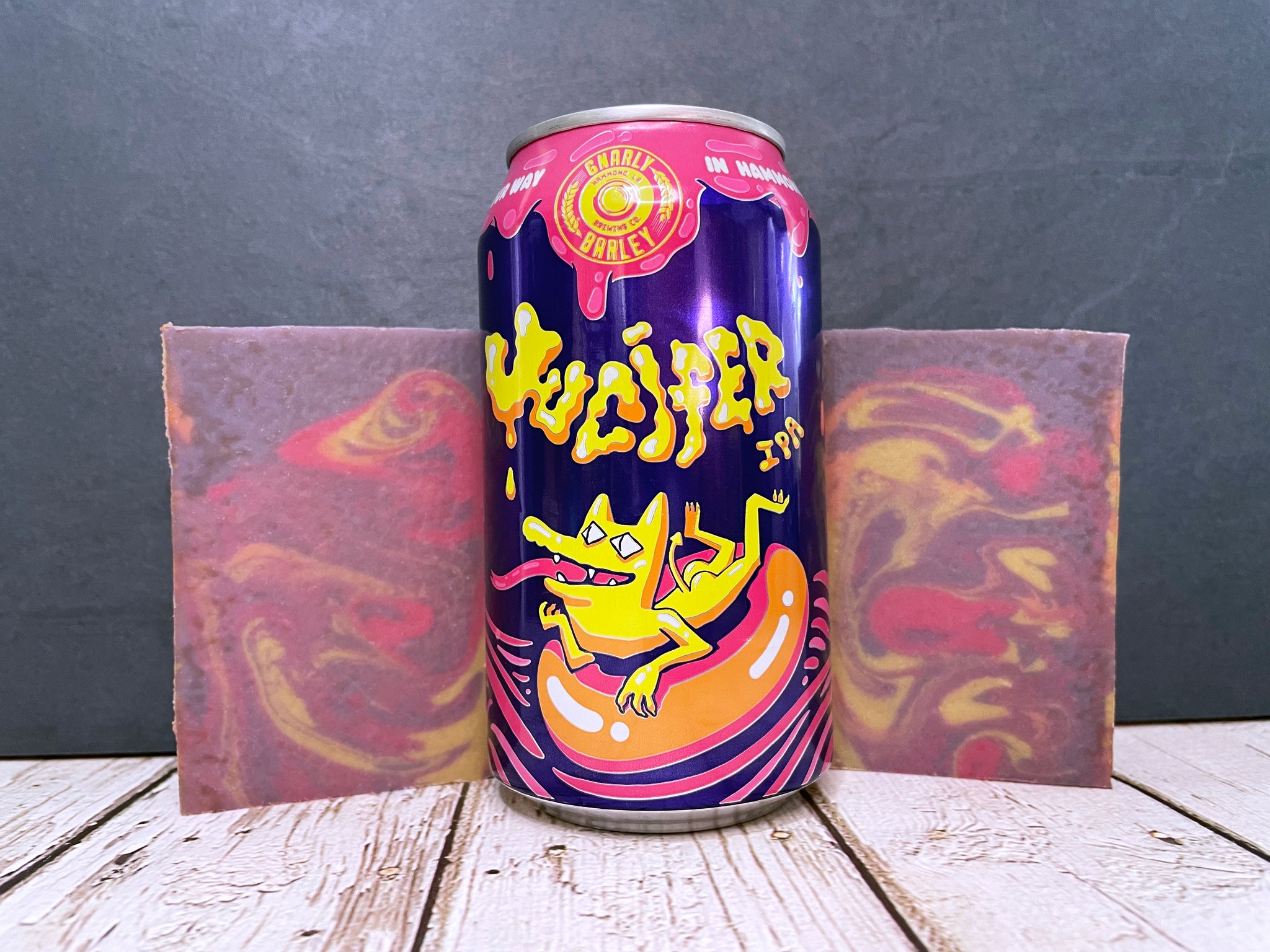 gnarly barley Jucifer IPA beer can between two bars of pink purple and yellow marbled beer soap on a wooden surface with stone background