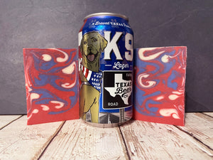 k9 lager Beer can with a dog illustration between two red and blue marbled beer soap bars on a wooden surface.