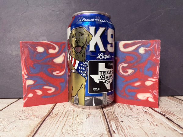 k9 lager Beer can with a dog illustration between two red and blue marbled beer soap bars on a wooden surface.