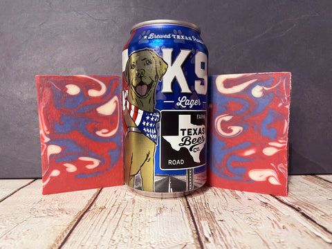 k9 lager Beer can with a dog illustration between two red and blue marbled beer soap bars on a wooden surface.