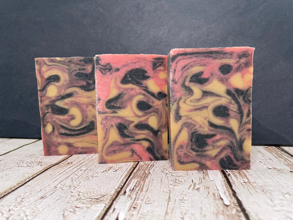Three swirled red gold and black beer soap bars on a wooden surface with a dark background