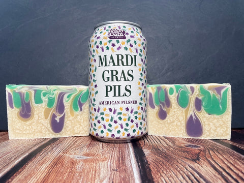 urban south brewery Mardi Gras pils American pilsner beer can between two bars of white purple gold and green swirl beer soap on a wooden surface