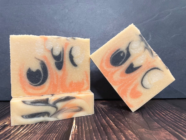 Three bars of beer soap with black, white, and orange swirls on a dark surface