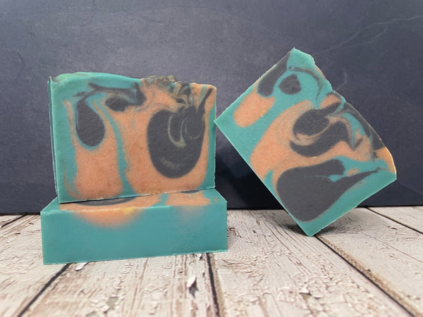 Three bars of beer soap with a teal and brown color pattern on a wooden surface.