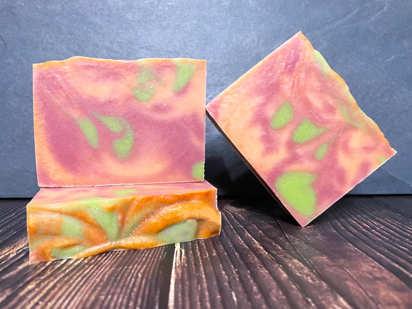 Three colorful beer soap bars with a pink, green, and orange pattern on a dark wooden surface with stone background