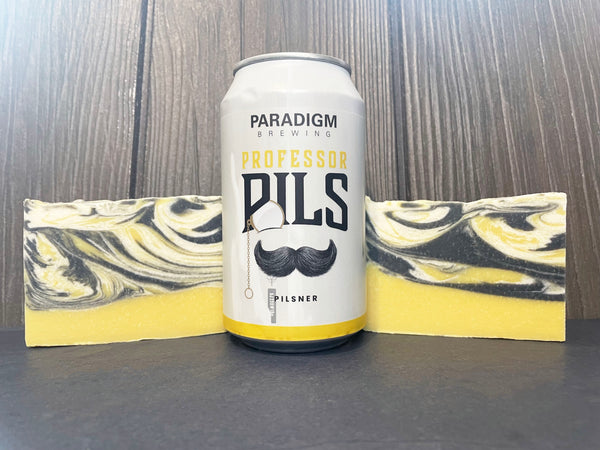 Can of Paradigm Brewing Professor Pils between two bars of beer soap on a wooden surface.