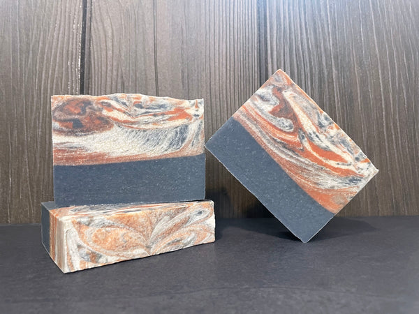 Three marbled red white and blue beer soap bars on a dark stone surface with a wooden background