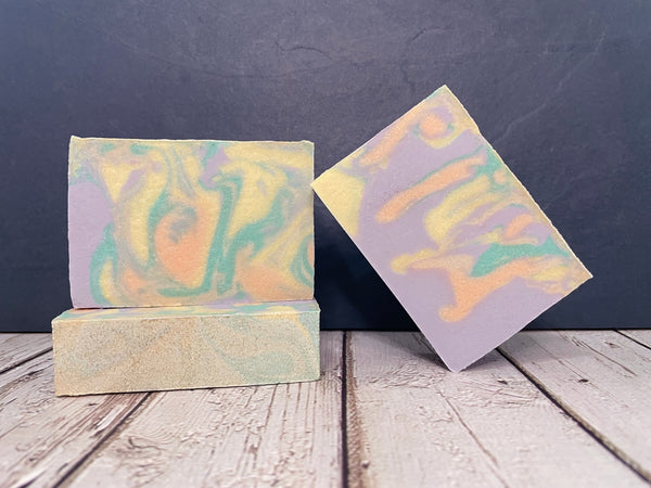 Three bars of yellow orange teal and purple beer soap on a wooden surface with a dark background