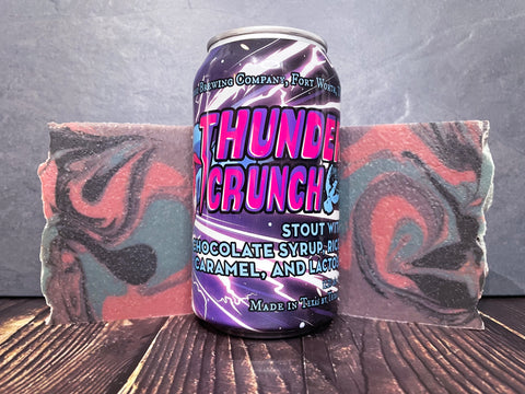 Martin House Brewing Company Beer Can of Thunder Crunch imperial stout with a colorful design between two bars of purple pink blue and black swirled beer soap bars on a wooden surface.