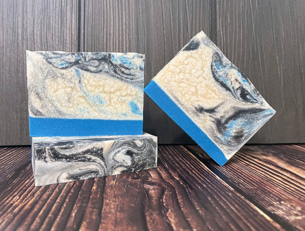 Three marbled beer soap bars with blue white and black patterns on a wooden surface.