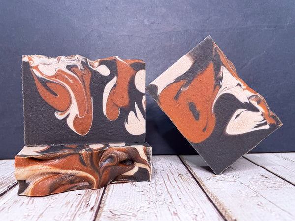 three bars of black chestnut and white beer soap on a wooden surface with a dark stone background