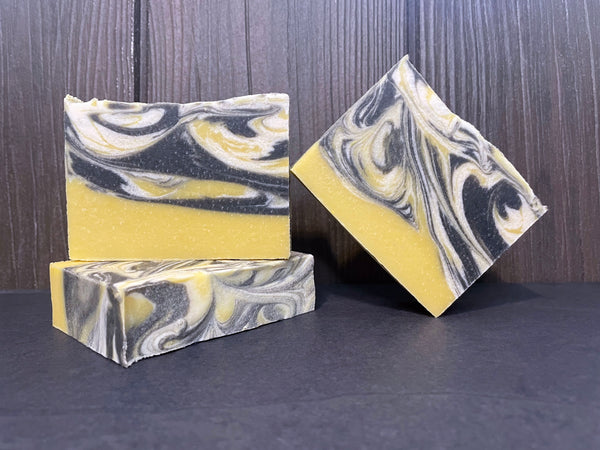 Three bars of marbled beer soap with yellow, black, and white colors on a stone surface.